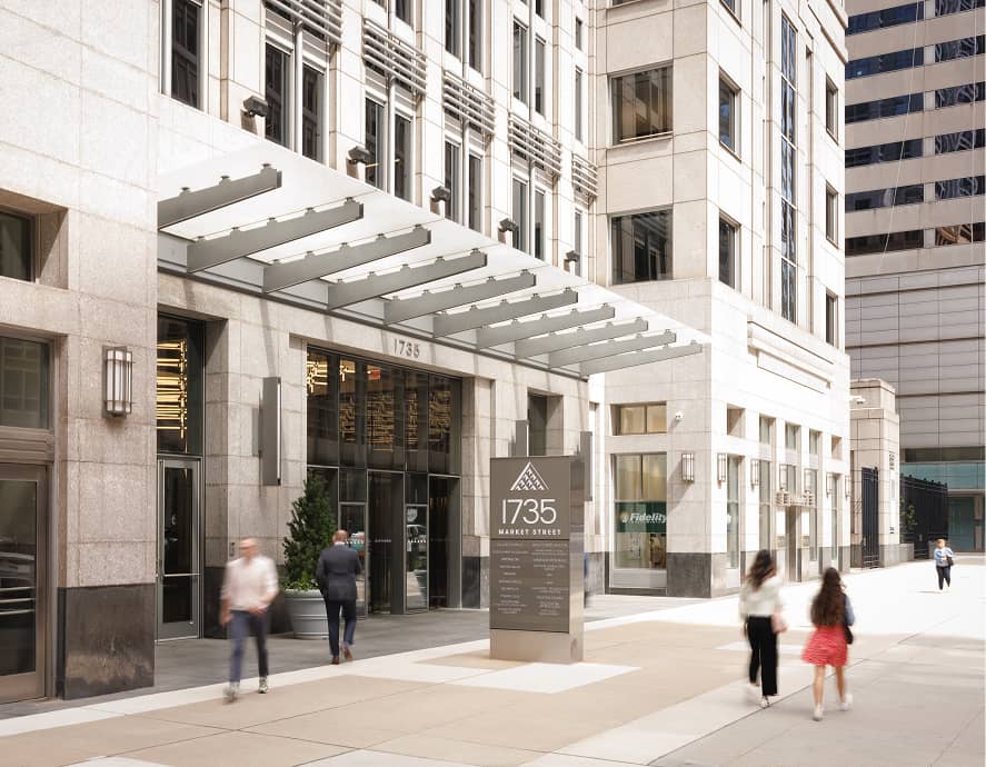 Urban scene with a modern building at 1735 Market Street. People walk on the sidewalk. The facade features glass and stone elements under a metal canopy.