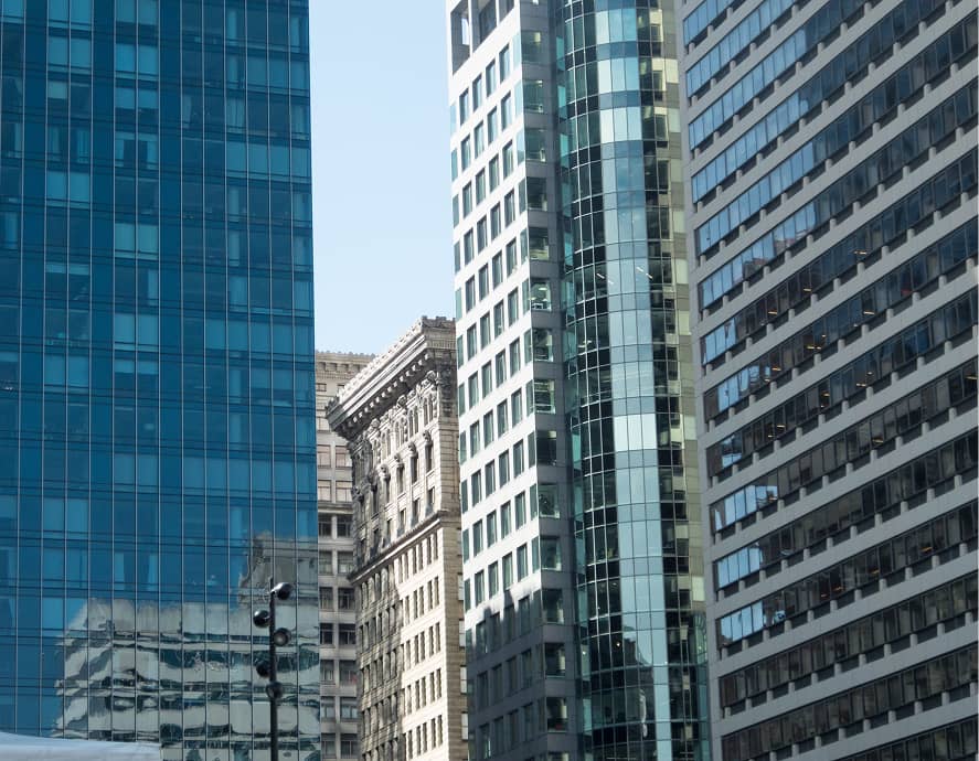 Cityscape featuring tall buildings against a clear sky; a mix of glassy modern skyscrapers and older, ornate stone architecture, conveying urban diversity.
