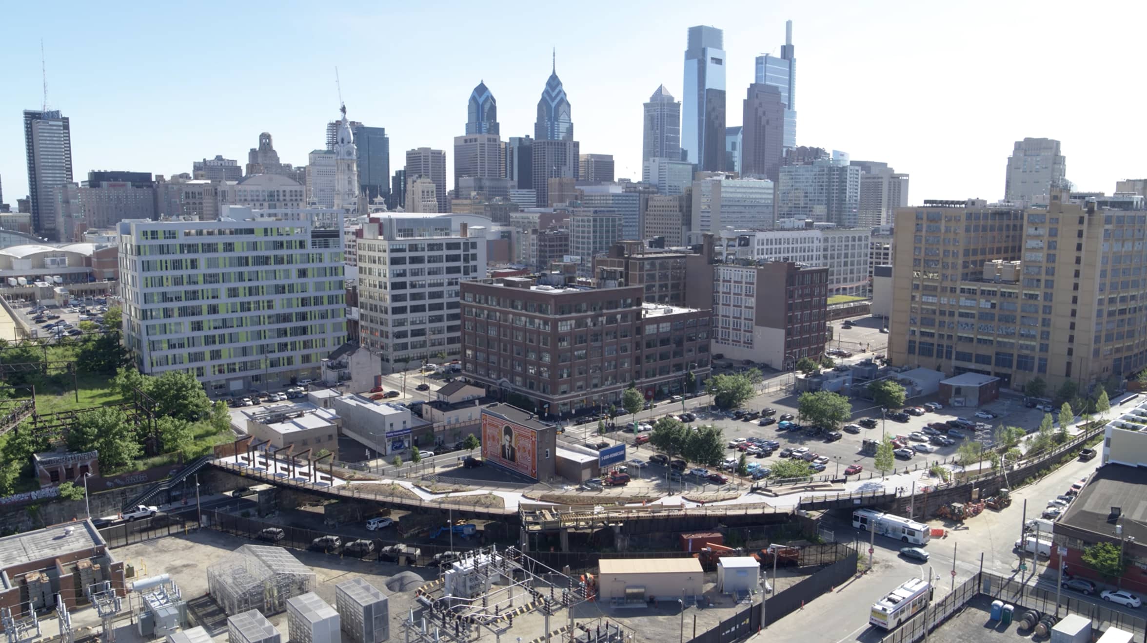 Aerial view of a cityscape featuring modern skyscrapers and historic buildings under a clear sky. A mural on a brick building adds artistic flair.