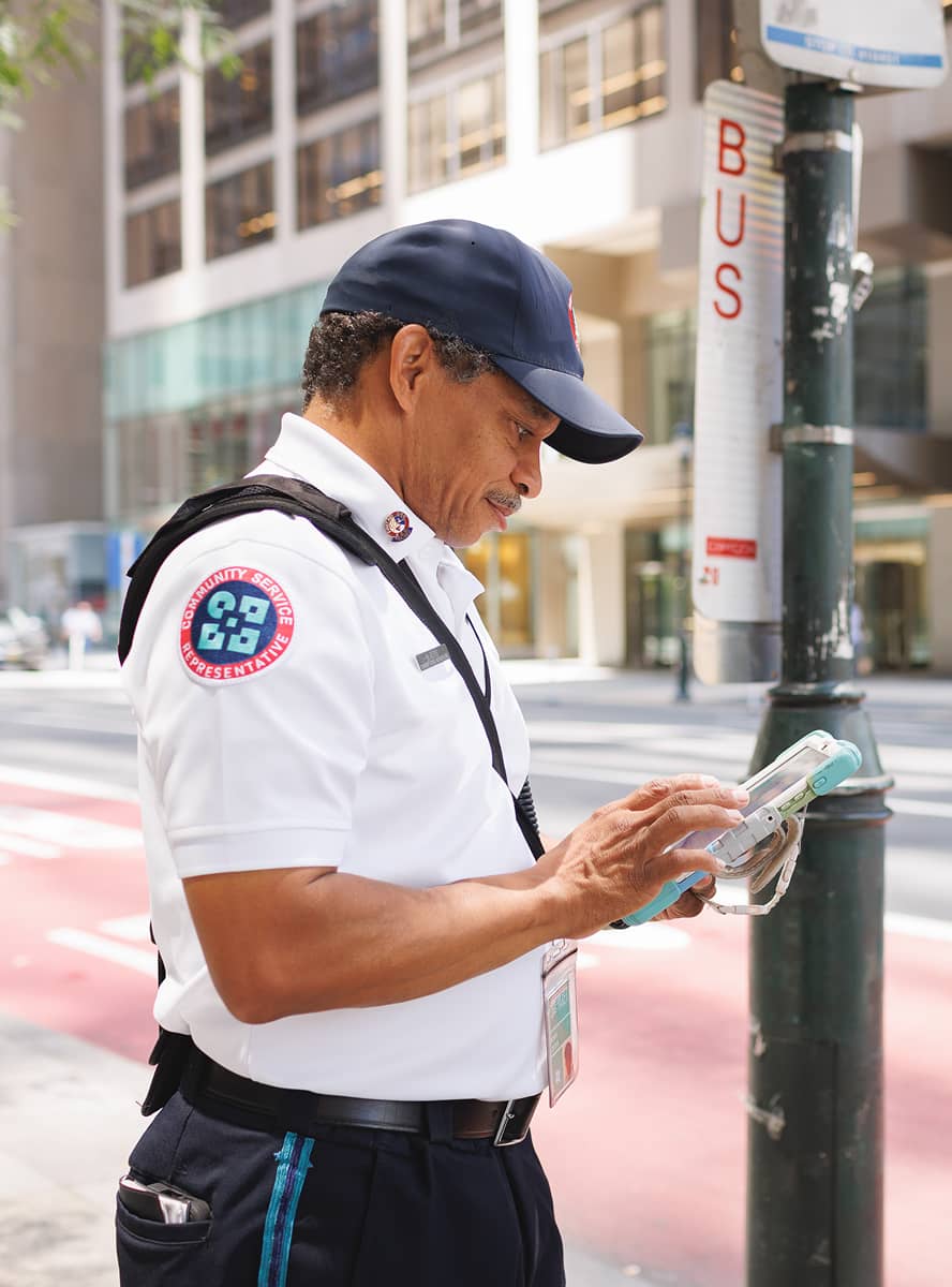 Security officer in a white uniform and cap stands by a street post labeled 