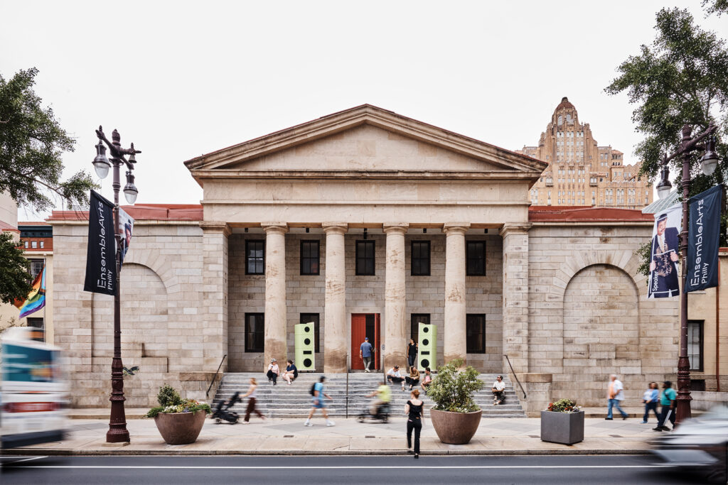 People walking by the sounds of Philadelphia sound installation on broad street at historic building with pillars.