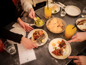 tacos drinks and chips on a table with people's hands digging in.