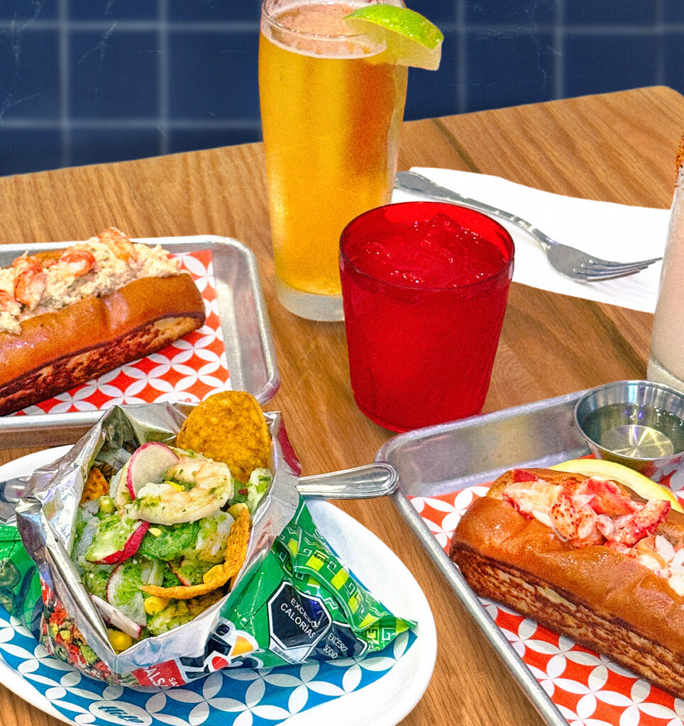 table scape with 2 lobster rolls, ceviche and beverages displaed