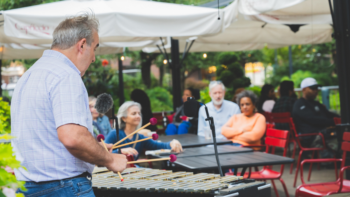 Man playing vibraphone in front of audience at outdoor cafe.