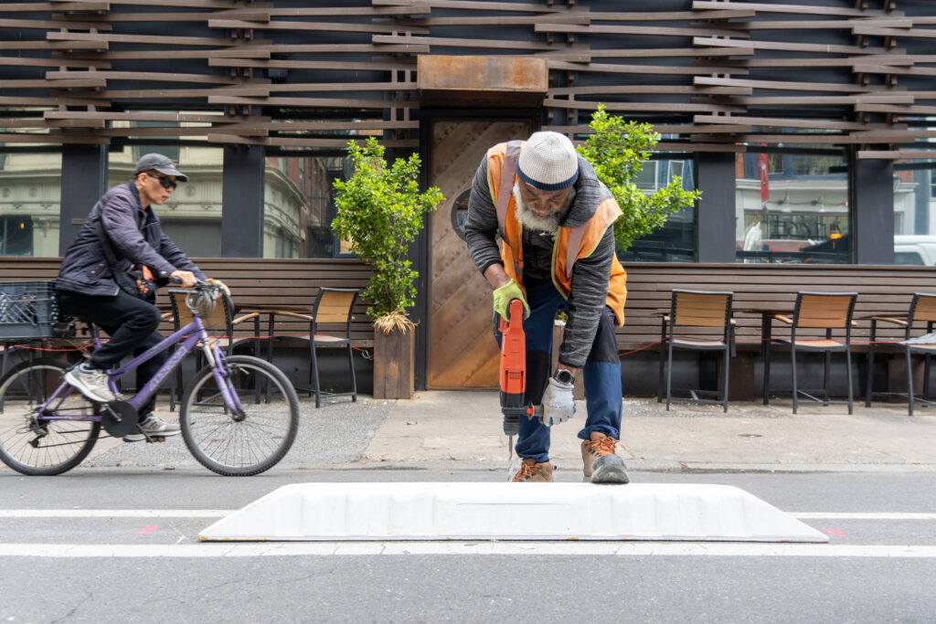 A city worker installing a plastic bike lane separator as a cyclist rides behind him.