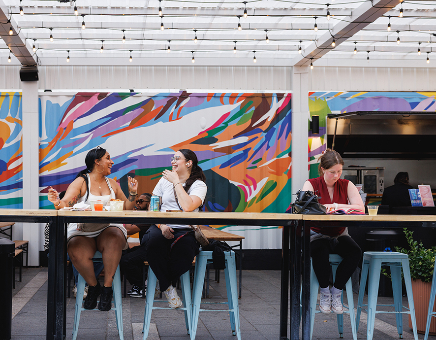 Women eating and talking at The Patio at Dilworth Park with the mural on the wall behind them.