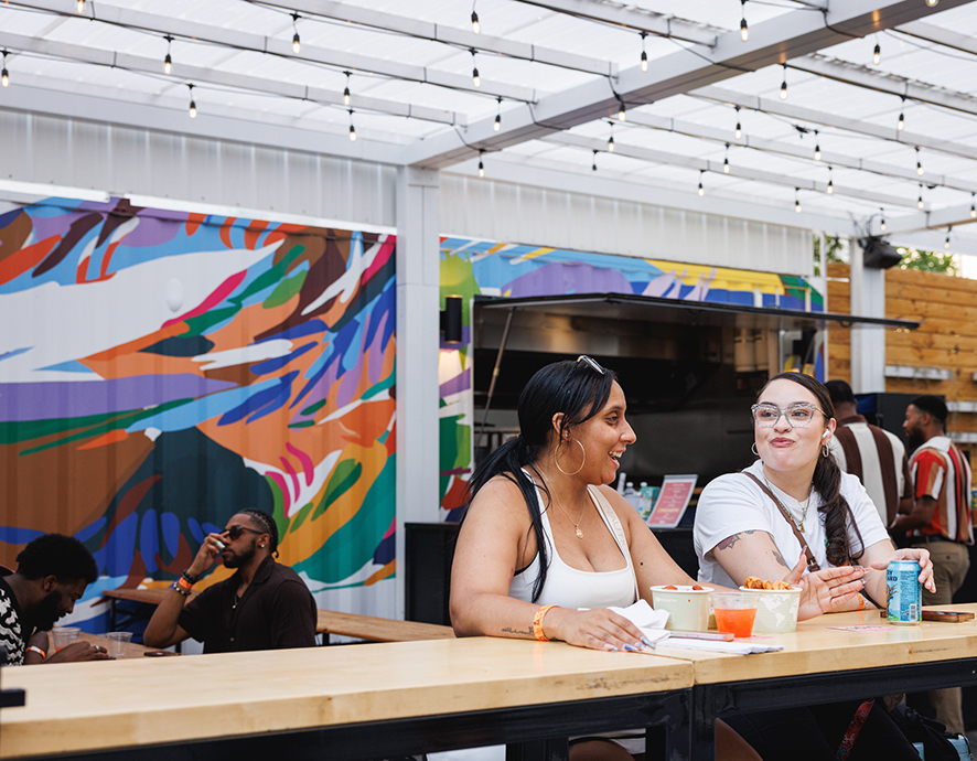Women eating and talking at The Patio at Dilworth Park with the mural on the wall behind them.