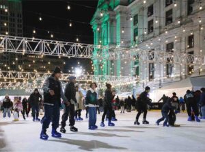 People skating at the Rothman Orthopaedics Ice Rink in Dilworth Park at night outside of Philadelphia's City Hall.